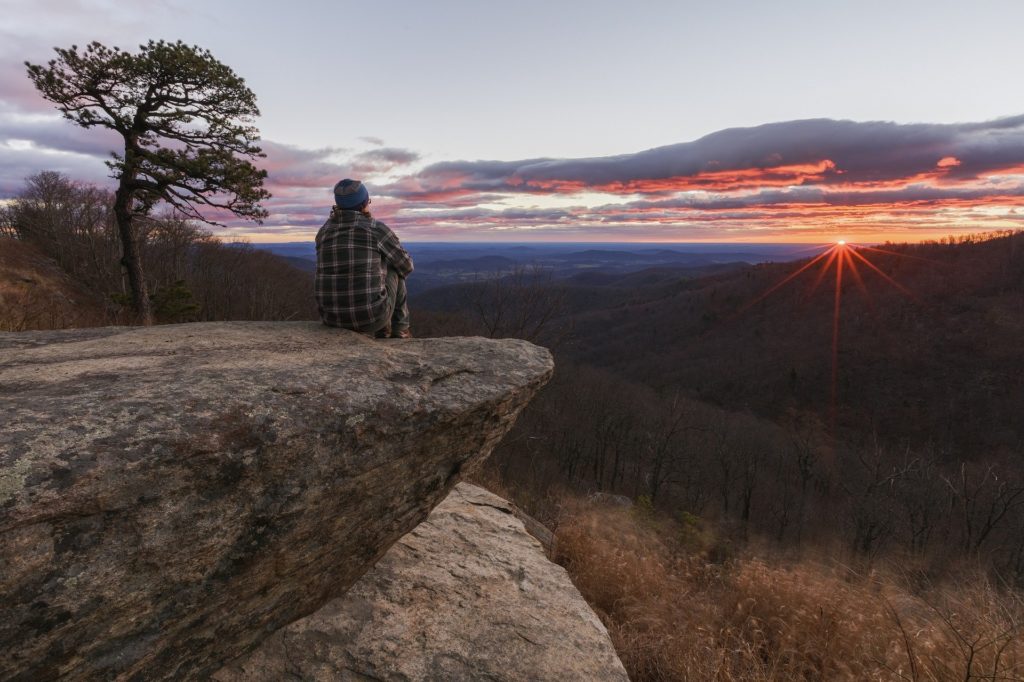 A person sits atop a mountain in Virginia overlooking the landscape and a beautiful sunset 