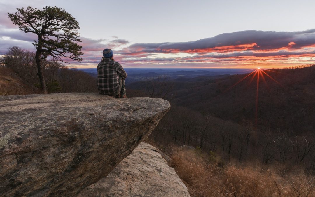 A person sits atop a mountain in Virginia overlooking the landscape and a beautiful sunset